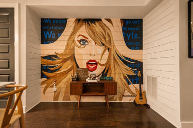 Pop-art mural of a surprised blonde woman with red lips and flowing hair on a shiplap wall, set above a mid-century console and electric guitar in a cozy Nashville-style interior