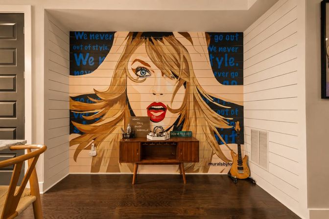 Pop-art mural of a surprised blonde woman with red lips and flowing hair on a shiplap wall, set above a mid-century console and electric guitar in a cozy Nashville-style interior