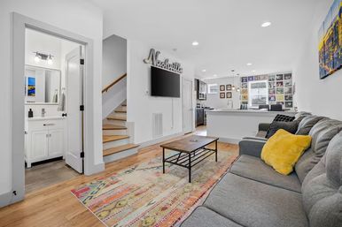 Bright modern Nashville open-plan living room and kitchen with gray sectional sofa, yellow accent pillow, colorful area rug, wall-mounted TV and stairway