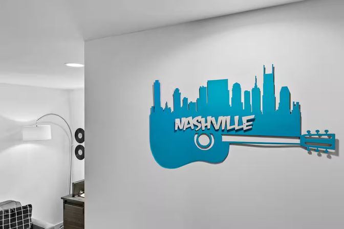 Blue Nashville skyline shaped like an acoustic guitar wall art on a white living room wall, modern floor lamp, vinyl records and side table visible