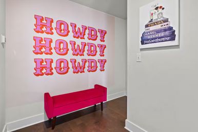 Modern foyer with retro pink-orange HOWDY wall decal repeated in three rows above a fuchsia upholstered bench, white walls and dark hardwood floor.