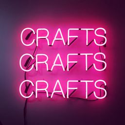 Triple pink neon 'CRAFTS' sign mounted on a wall, bold magenta glow and retro craft-studio decor.