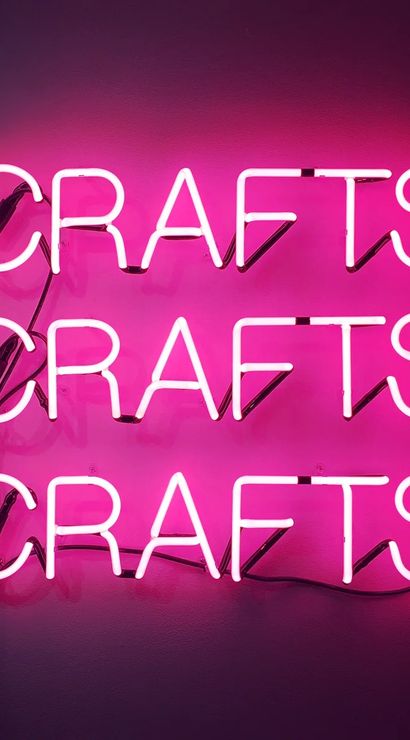 Triple pink neon 'CRAFTS' sign mounted on a wall, bold magenta glow and retro craft-studio decor.