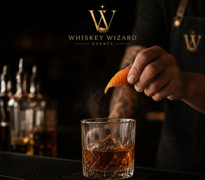 Close-up of a bartender squeezing an orange peel over an Old Fashioned — citrus oil misting onto amber whiskey in a cut-glass tumbler with a large ice cube on a dark bar