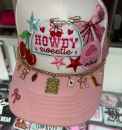 Pink trucker cap with embroidered "HOWDY sweetie" patch, cherries, stars and bow accents, decorated with a gold charm chain of tiny trinket charms