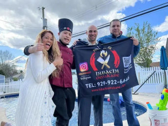 Four smiling adults at a suburban backyard pool giving thumbs up while holding a black hibachi catering banner at an outdoor teppanyaki pop-up
