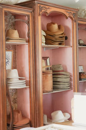 Stacks of tan, white and woven straw cowboy hats displayed on vintage wooden shelves with a pink-painted backing.