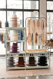 Sunlit boutique shop window showing stacked felt hats on shelves and hanging decorative hatbands.