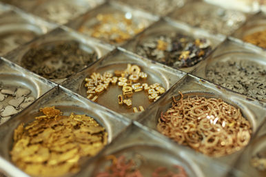Close-up of a metal organizer tray filled with gold and bronze jewelry components — small charms, crystal-studded letter beads and jump rings for DIY jewelry making