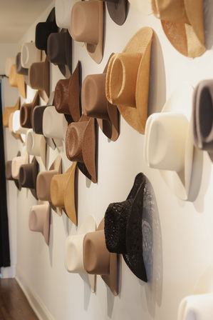 Stylish wall display of neutral-toned fedoras and straw hats in beige, brown, black and cream neatly arranged on a white boutique interior wall