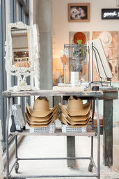 Bright home-decor boutique display with stacked straw cowboy hats on a rustic metal table, ornate white mirror and design books