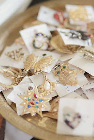 Gold-tone brooches and pins on a decorative tray — jeweled star, butterfly, owl and pearl-accented pieces on white display cards, boutique jewelry display