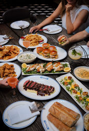 Restaurant table spread of American shared plates: mini burgers, fries, sliced steak with sauce, seared scallops, fried chicken, bread, dips and cocktails.