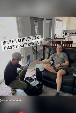 Person relaxing on a living room recliner receiving mobile IV drip from a technician kneeling with a medical kit — in-home IV therapy and wellness service near the kitchen.