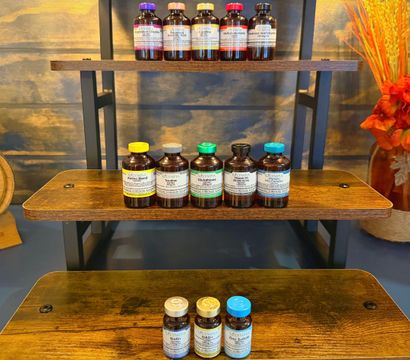 Tiered wooden shelf displaying amber supplement vials with colorful caps, small wooden barrel and bright orange floral arrangement — wellness display