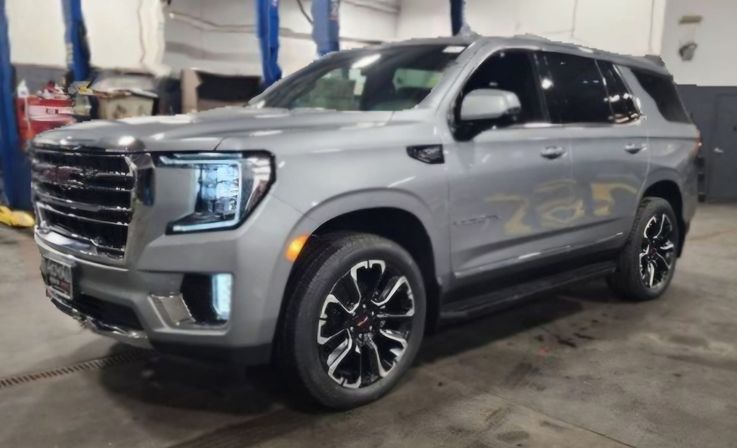 Shiny silver full-size SUV parked in an indoor auto service garage with LED headlights on and black alloy wheels.