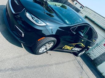 Sleek black sedan parked in an urban alley, angled close-up showing the front wheel and passenger side with bright yellow transportation-service graphics.