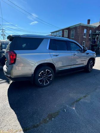 Gleaming silver full-size SUV parked on an urban street beside red brick buildings under a bright blue sky
