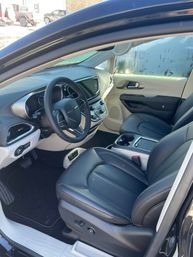 Front interior of a modern SUV parked in a snowy lot — black leather driver and passenger seats, leather-wrapped steering wheel, touchscreen center console, dual cup holders and light two-tone trim.
