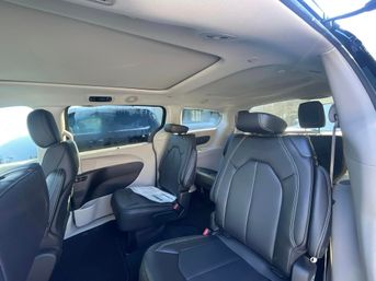 Spacious minivan interior with black leather captain seats, white contrast stitching, large side windows, light gray headliner and open sliding door letting daylight into the second-row seating.