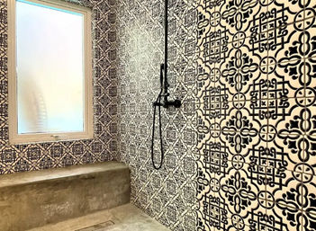 Modern walk-in shower with matte black wall-mounted fixtures, bold black-and-white geometric patterned tiles, concrete bench and frosted window