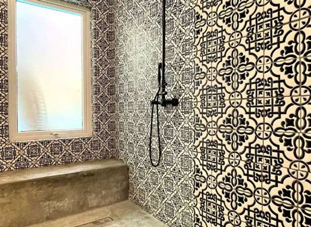 Modern walk-in shower with matte black wall-mounted fixtures, bold black-and-white geometric patterned tiles, concrete bench and frosted window