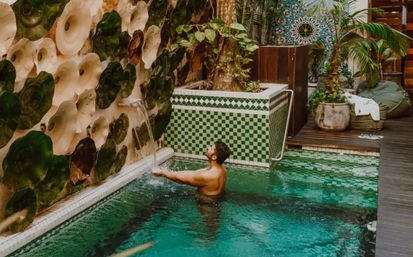 Man enjoying a small outdoor tiled plunge pool with green mosaic tiles and a decorative waterfall wall in a tropical courtyard