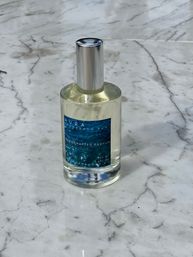 Clear glass perfume bottle with a silver cap and blue ocean-pattern label, standing on a white marble countertop.