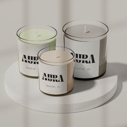 Three minimalist scented candles in clear glass jars—pastel green, blush, and gray—arranged on a white round display stand under soft natural light, modern tabletop home decor.