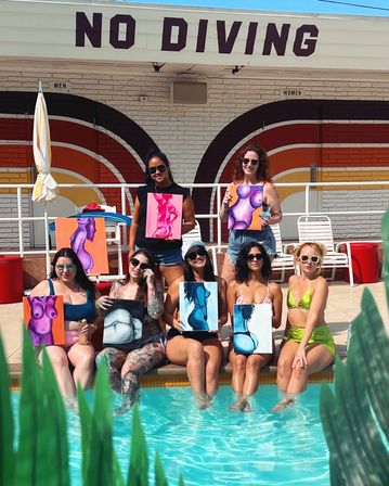 Group of seven women in swimsuits at a sunny outdoor poolside painting party, feet in turquoise water under a large 'NO DIVING' sign, each holding colorful abstract canvases of female torsos against a retro striped wall.