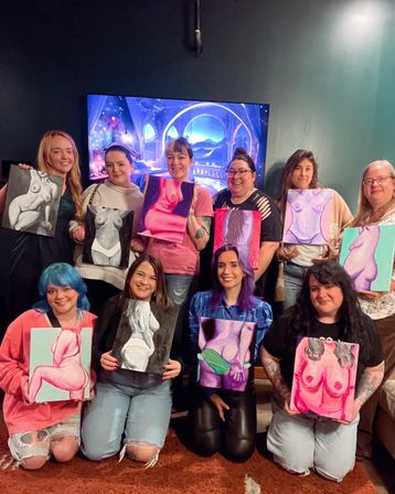 Group paint‑night in a cozy indoor art studio: a smiling group holding colorful canvases of stylized nude figures in front of a decorative screen, playful women’s painting party.