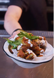 Crispy battered vegetable bites drizzled with creamy ranch and paprika, garnished with fresh parsley in a white enamel bowl being handed across a restaurant counter