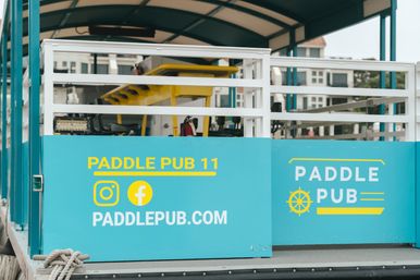 Teal pedal-powered party boat docked at a marina with white railings, yellow seating and social media icons on the side panel.