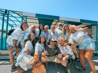 Cheerful group of friends in matching tie-dye shirts posing on a sunny waterfront ferry pier, smiling and ready for a beach trip