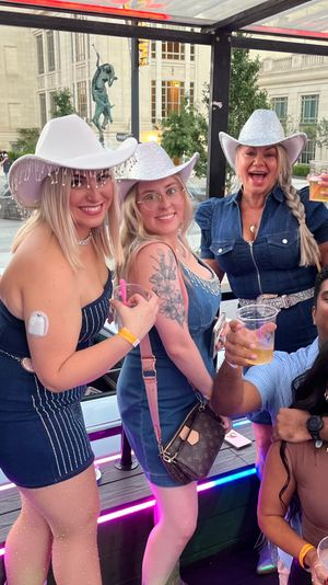 Friends in sparkly silver cowboy hats and denim on an open-air party trolley downtown, smiling and holding drinks near a civic building