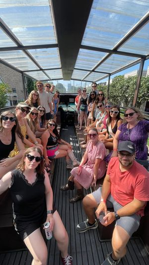 Cheerful group of people on an open-air covered party trolley, wearing summer clothes and sunglasses, riding down a sunny residential street.