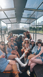 Group of women in denim, cowboy hats and boots celebrating on an open-air party bus with a downtown city skyline in the background