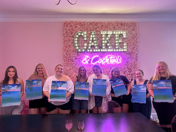 Paint-and-sip party: a group of attendees holding tropical beach canvases in front of a pink floral wall with a lit marquee "CAKE" sign and neon "& Cocktails".