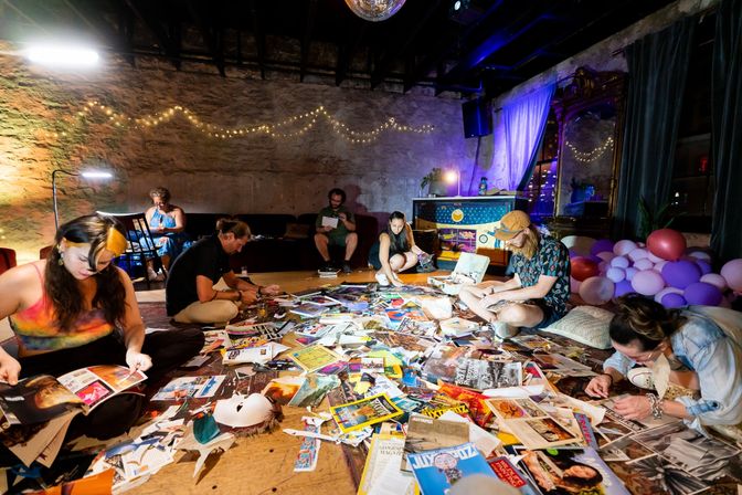Creative collage workshop in an urban loft studio — six people seated on the floor surrounded by scattered magazines, cutouts and art supplies under string lights and a disco ball, with balloons and a vintage mirror in the background.