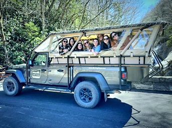 Smiling group on open-air safari jeep tour along a scenic forest mountain road