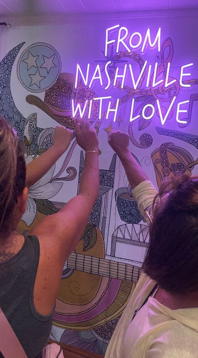 Three people seen from behind raising fists toward a purple neon sign reading "FROM NASHVILLE WITH LOVE" over a colorful guitar-and-music-note mural