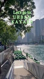 Green kayaks lined up on a riverfront dock with a person launching into a sunny downtown waterway, leafy trees and high-rise skyline; text overlay invites a kayak outing.