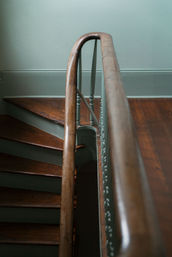 Close-up of a vintage wooden staircase interior featuring a curved polished banister, painted balusters, and worn hardwood treads