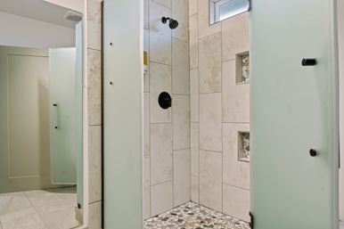 Bright, spa-like tiled walk-in shower with pebble mosaic floor, built-in niches, matte black shower fixtures and frosted glass doors in a modern bathroom