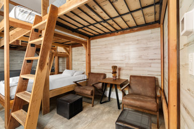 Cozy cabin-style interior with sturdy wooden bunk beds and ladder, twin beds, light wood plank walls, two brown leather armchairs, small wooden table and leather ottomans.