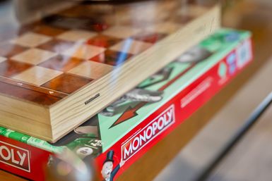 Close-up of a wooden chessboard stacked on a red Monopoly game box on a glass table, colorful game graphics and shallow depth of field.