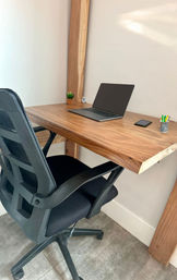 Cozy minimalist home office corner with a live-edge wooden desk and timber post, black mesh swivel chair, open laptop and smartphone, small potted succulent and pencil cup on tiled floor.