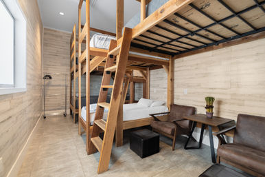 Cozy modern-rustic shared room with stacked wooden bunk beds and ladder, leather armchairs, small table and light wood-paneled walls
