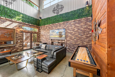 Modern industrial urban loft living/game room with leather sectional, brick accent wall, wall-mounted TV, indoor shuffleboard table, tall clerestory windows and green plant trim