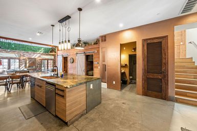 Open-concept modern-rustic loft kitchen with wood island and stone countertop, industrial pendant lights, exposed brick dining wall with living green wall, sliding barn doors, concrete floors and wooden staircase.